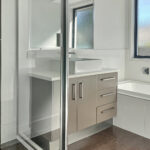 Modern bathroom with a white vessel sink on a gray vanity, frosted window, and subway tile walls revolving around a glass shower door.