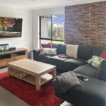 Cozy living room with gray sectional sofa, red shag rug, brick accent wall, and wooden coffee table; TV mounted on wall.