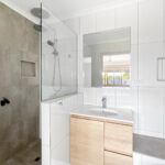 Modern bathroom with a glass shower enclosure, white tiled walls, and a wooden vanity under a mirror.