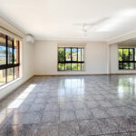 Bright empty living room with large windows, tiled floor, white walls, and a ceiling fan.