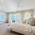 Bright modern bedroom with a large striped bed, neutral tones, and sheer curtains facing sliding doors to a balcony view