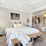 Bright master bedroom with striped duvet, cream bed, wicker pendant lights, blue nightstand, and an open walk-in closet.