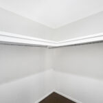 Empty walk-in closet with white walls, two metal hanging rods along the sides, and a single hanger on the right side.