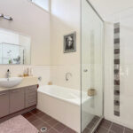 Modern bathroom with gray vanity, white sink, large mirror, and glass-enclosed shower area.