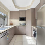 U-shaped modern kitchen with beige cabinets, stainless steel fridge, microwave, toaster, and a double sink under a large front window.