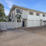 Modern white townhouse complex with multiple garages and a paved driveway under a clear blue sky.