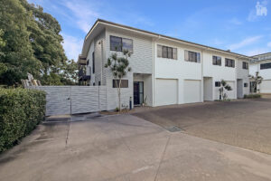 Modern white townhouse complex with multiple garages and a paved driveway under a clear blue sky.