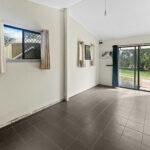 Empty living area with gray tiled floor and large sliding glass door to a lawn and trees outside, curtains on windows, and a hanging light bulb.