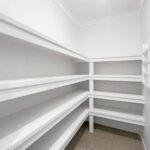 Empty white pantry with multiple built-in shelves and a partially open door; ample storage space shown.