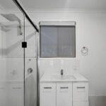 Modern bathroom with glass shower enclosure, white vanity, and small window in a gray-toned room.