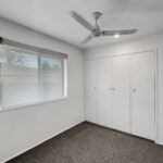 Empty room with a window on the left, white walls, a ceiling fan, and a row of white built-in closets on the right.