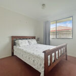 Bedroom with a wooden bed and floral bedding, brown carpet, and a large window showing a blue sky outside